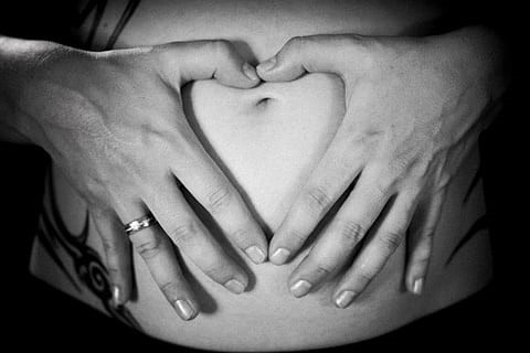 Hands in the shape of a heart over a pregnant belly