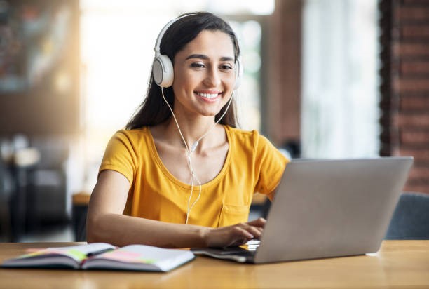 Young woman with headphones on smiling while looking at her computer