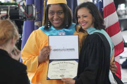 Photo of a girl in a cap and gown recieving her diploma from a woman at graduation