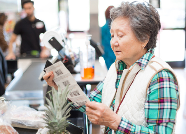 senior woman looking at her coupons before paying for her groceries