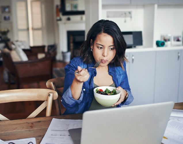 Woman sitting at computer eating a salad while working