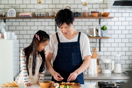 A man and a little girl engage in cooking activities together in a warm, family-friendly kitchen setting.