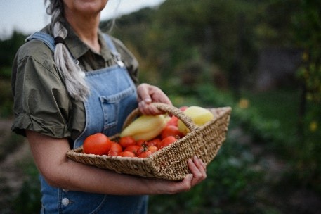 A woman with a joyful expression, carrying a basket overflowing with vibrant, fresh vegetables.