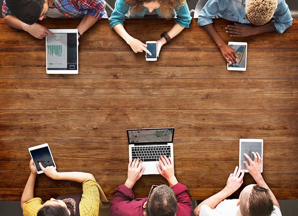 People sitting on a table and working with phones, tablets, and laptops People sitting on a table and working with phones, tablets, and laptops