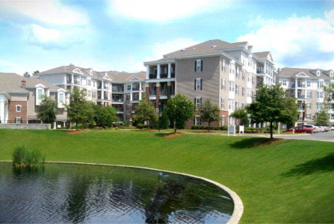 Apartment complex with a lawn and pond in the foreground.